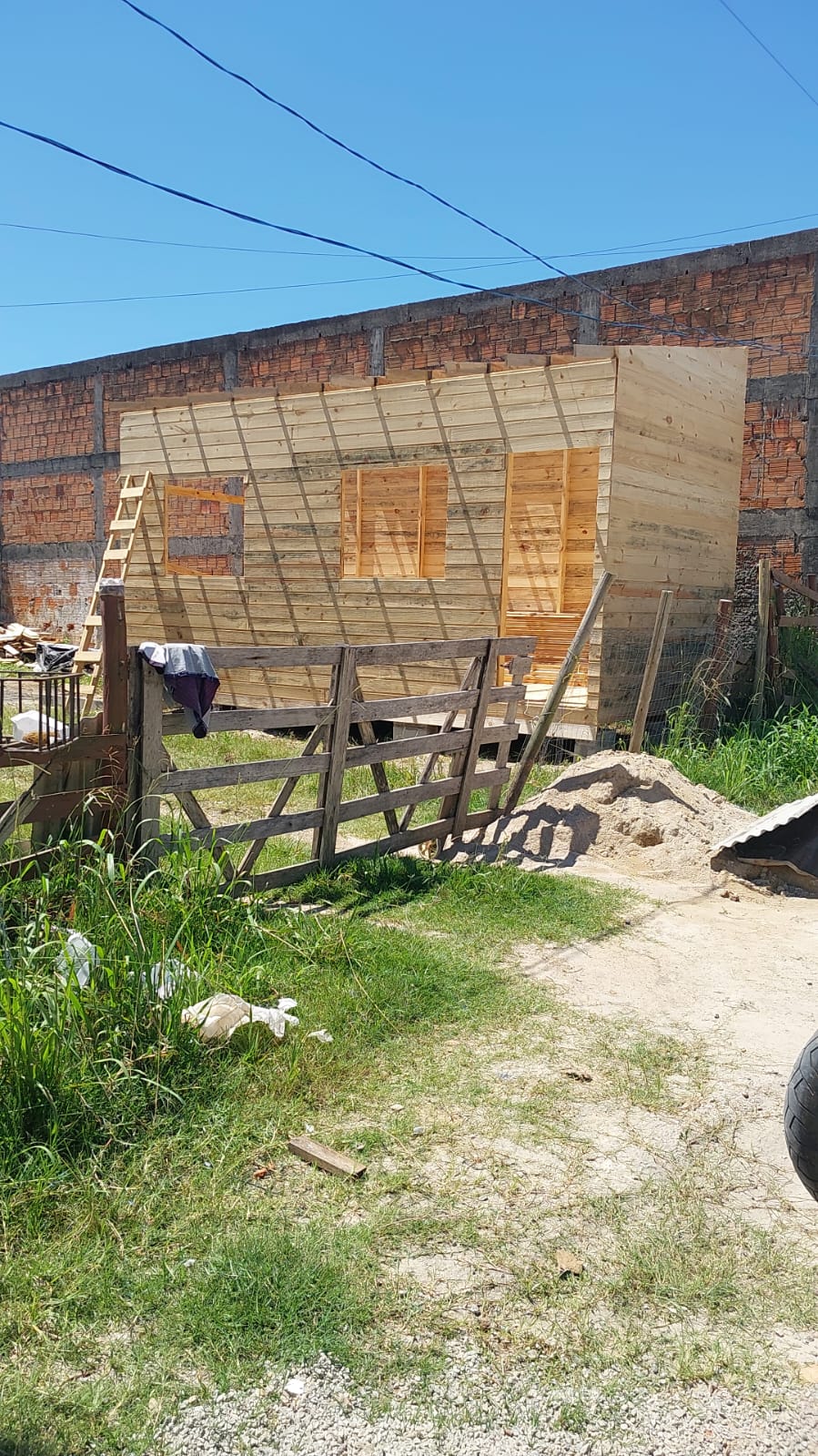 Construção de uma cabana de madeira em um terreno com barreira de madeira, areia e paredes de tijolo no fundo