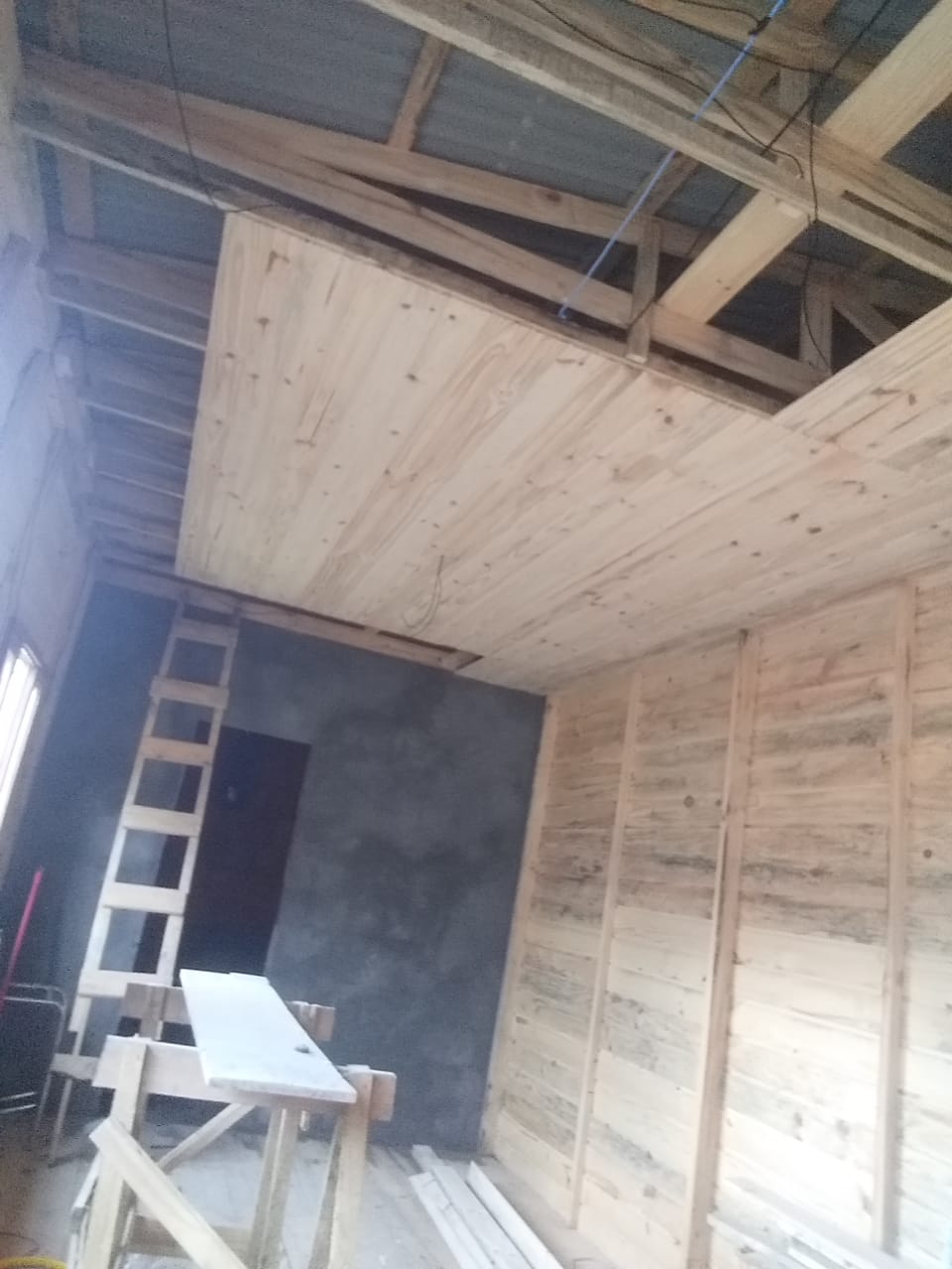 Interior de construção em andamento com madeira, lousa, escada de madeira e ferramentas